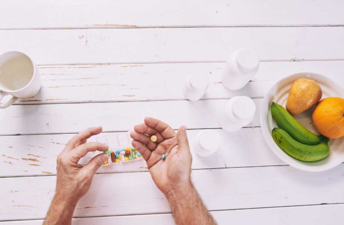 A close-up of a person sorting colorful daily supplements next to fresh fruit and white pill bottles, representing a morning vitamin routine to support circulation and wellness.