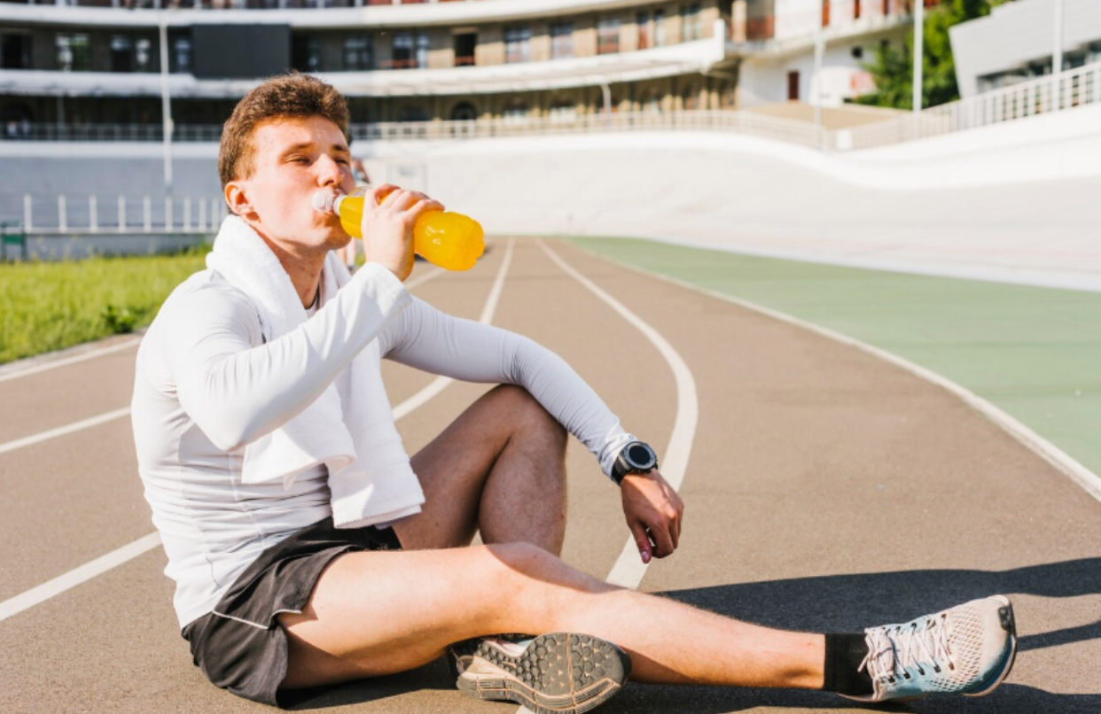 Male athlete drinking a bright recovery beverage on a track after training, symbolizing mitochondrial support for endurance and faster recovery.