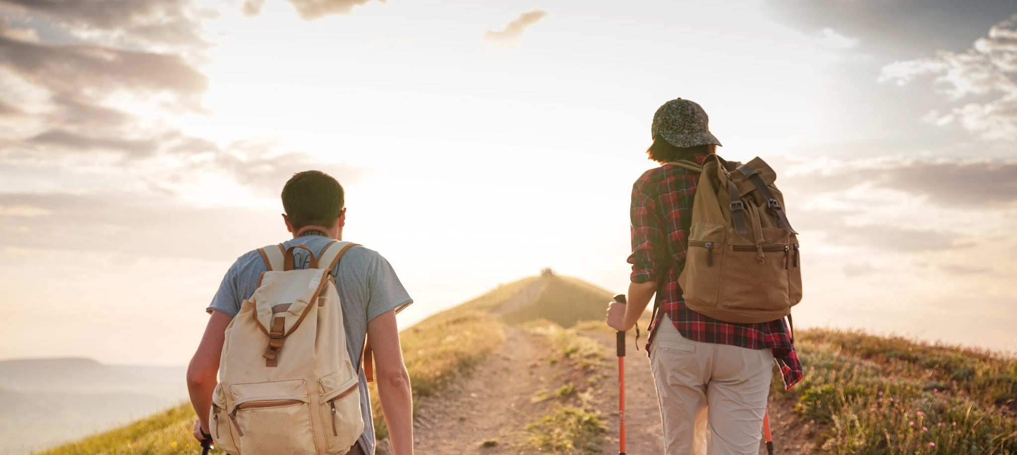 Two hikers with backpacks walking on a trail with a scenic background